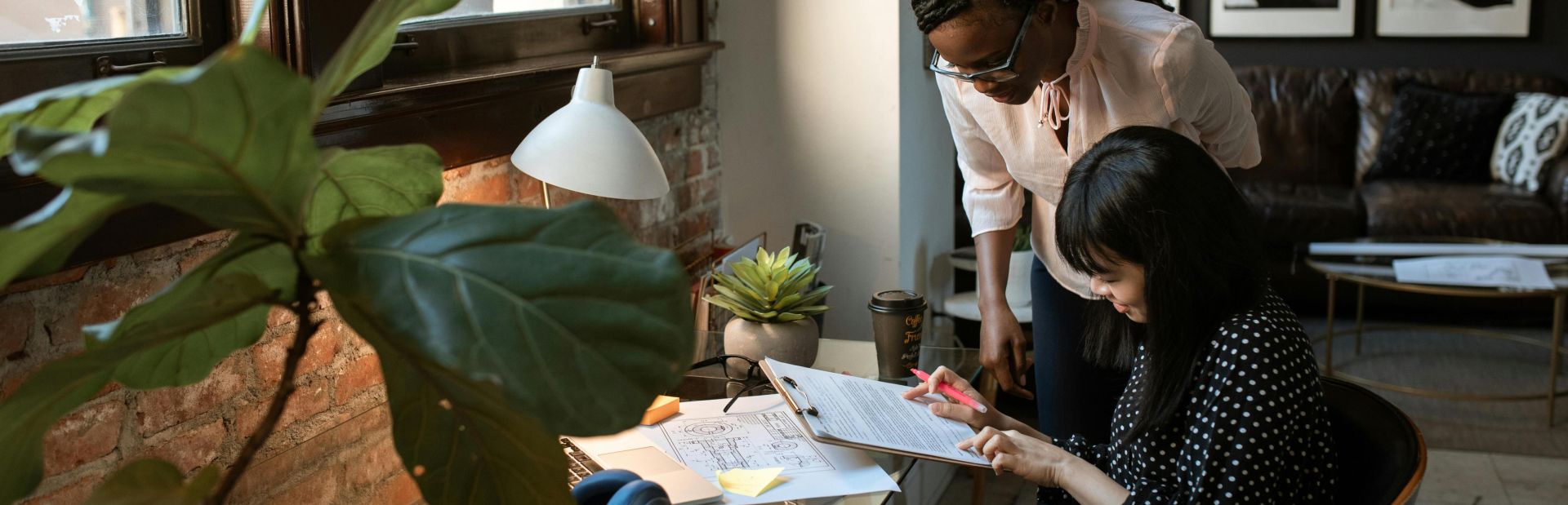 Two colleagues collaborate in a stylish, plant-filled workspace with natural light.
